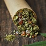 An open pre-roll spilling out cannabis flower, amber concentrates, and crystalline diamonds onto a wooden surface.