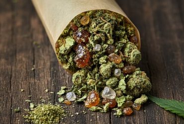 An open pre-roll spilling out cannabis flower, amber concentrates, and crystalline diamonds onto a wooden surface.